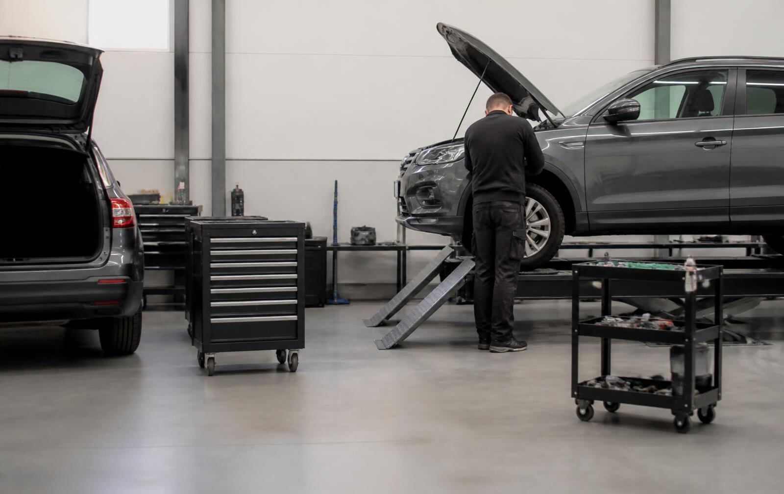 Technician working at a vehicle raised on a ramp in a clean service workshop with tool trolleys